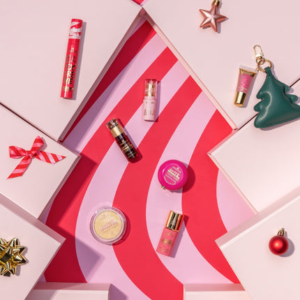 Essence Dancing Around The Xmas Tree collectie met mascara, lip beautifier, lip stain, peptide lip mask, highlighter, liquid blushlighter en mini lipgloss met kerstboomhanger op een roze-rode kerstboomachtergrond